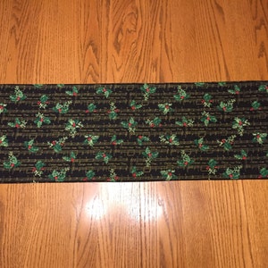 May include: Black table runner with a gold and green Christmas music and holly design.