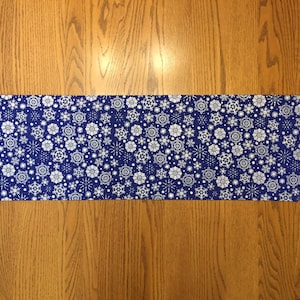 May include: A blue table runner with a white snowflake pattern.