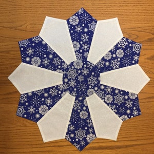 May include: A blue and white snowflake patterned table runner with a starburst design. The runner is made of fabric with a subtle glitter finish.