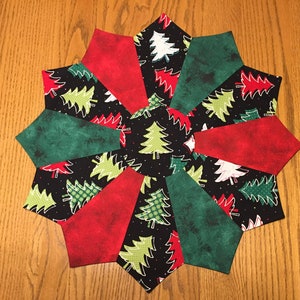 May include: A Christmas-themed table runner with a black background and a repeating pattern of green and white Christmas trees. The runner is made of fabric and has a starburst design with alternating red and green fabric panels.