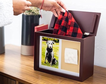 Puede incluir: Una caja de madera marrón oscuro con tapa con bisagras, que incluye dos marcos de fotos y un pequeño compartimento. La caja contiene una tela de cuadros rojos y negros y una huella de pata blanca. Los marcos de fotos muestran una foto de un perro y una huella de pata.