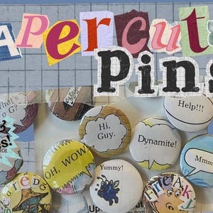 May include: A collection of colorful papercut pins with various phrases and illustrations. The pins are 1.25 inches in diameter and feature text like "Hi, Guy," "Dynamite!," and "Mmmm." The background includes the words "Papercut Pins" in a collage style.