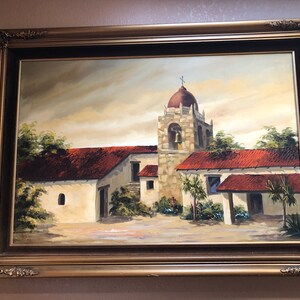 May include: Oil painting of a mission-style building with a bell tower and red tile roof, set in a landscape. The painting is framed in a gold ornate frame.