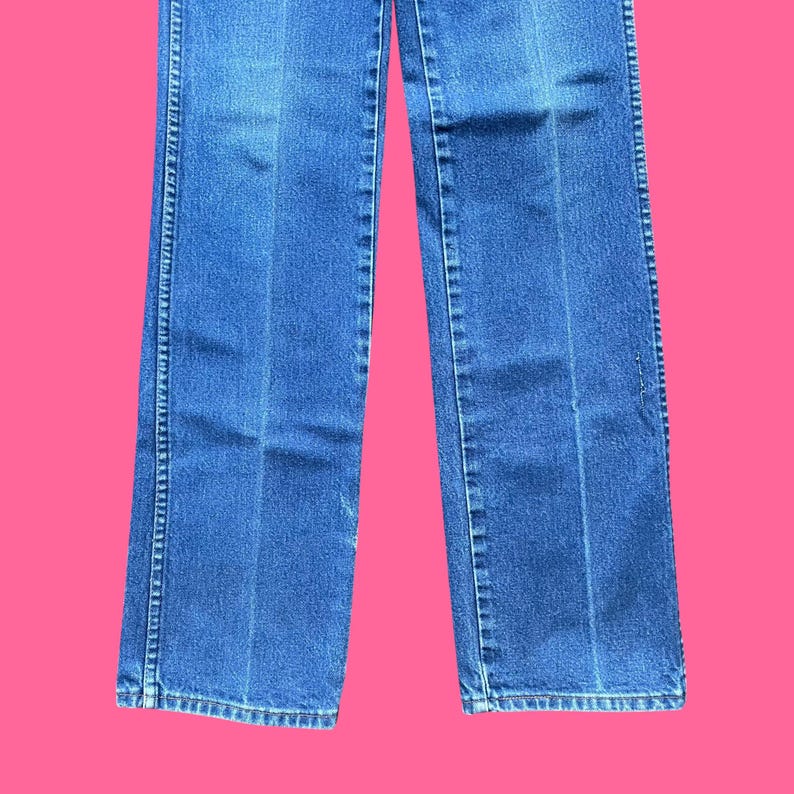 May include: Blue denim jeans with a straight leg cut. The jeans have a classic five-pocket design, a zipper fly, and a button closure. The jeans are a medium wash and have a slight fade.