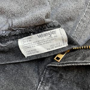 Puede incluir: Primer plano de unos vaqueros Wrangler negros. La etiqueta muestra la marca e instrucciones de lavado. Los vaqueros son talla 30 x 36 pulgadas, fabricados en EE. UU. con 100% algod&oacute;n. Se ve una cremallera dorada.