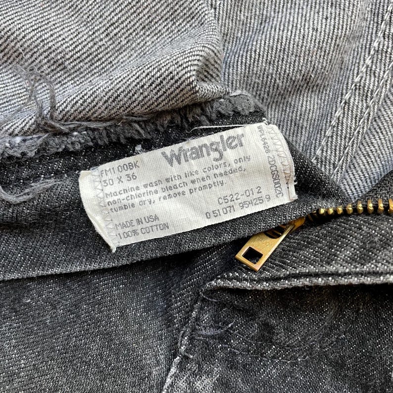 Puede incluir: Primer plano de unos vaqueros Wrangler negros. La etiqueta muestra la marca e instrucciones de lavado. Los vaqueros son talla 30 x 36 pulgadas, fabricados en EE. UU. con 100% algod&oacute;n. Se ve una cremallera dorada.