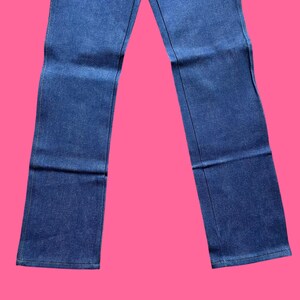 Op de afbeelding: Een spijkerbroek van blauwe denim. De jeans heeft een klassiek ontwerp met vijf zakken, met een rechte pijp. De denim is een medium wassing en de jeans heeft een knoop- en ritssluiting. De jeans wordt getoond tegen een roze achtergrond.