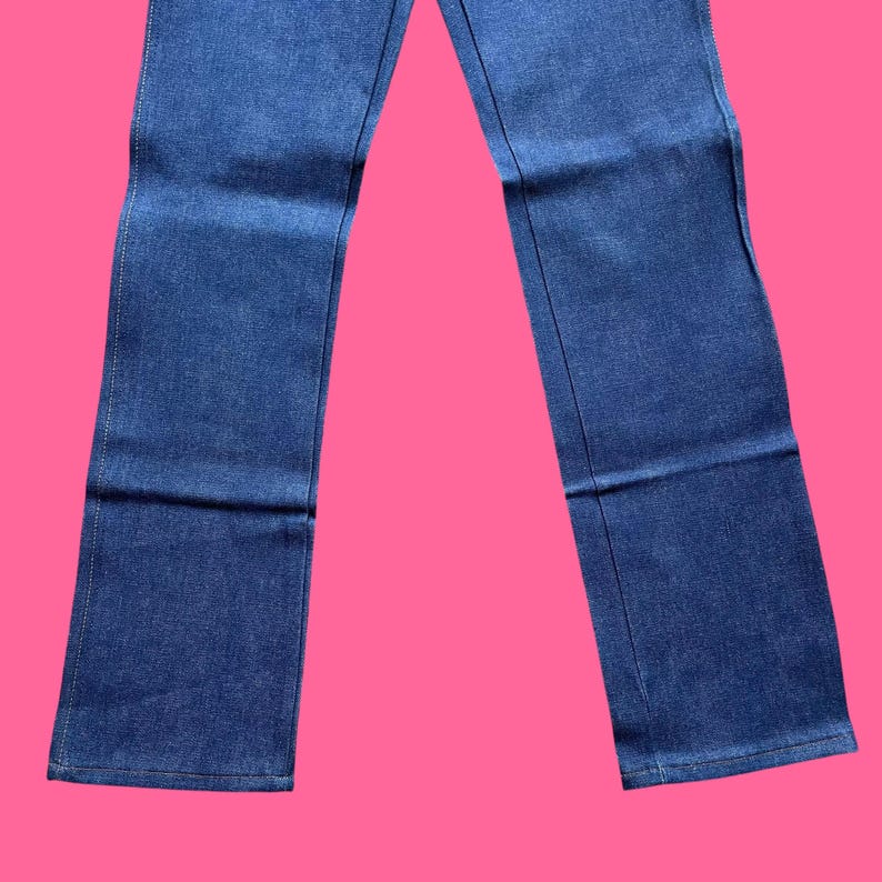 Op de afbeelding: Een spijkerbroek van blauwe denim. De jeans heeft een klassiek ontwerp met vijf zakken, met een rechte pijp. De denim is een medium wassing en de jeans heeft een knoop- en ritssluiting. De jeans wordt getoond tegen een roze achtergrond.