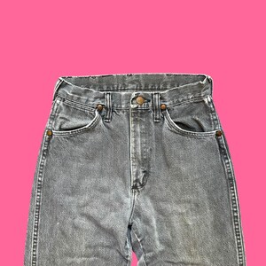 May include: Close-up of gray denim jeans with a high waist. The jeans have classic five-pocket styling, a button and zipper closure, and copper-colored rivets. The denim has a slightly faded appearance.