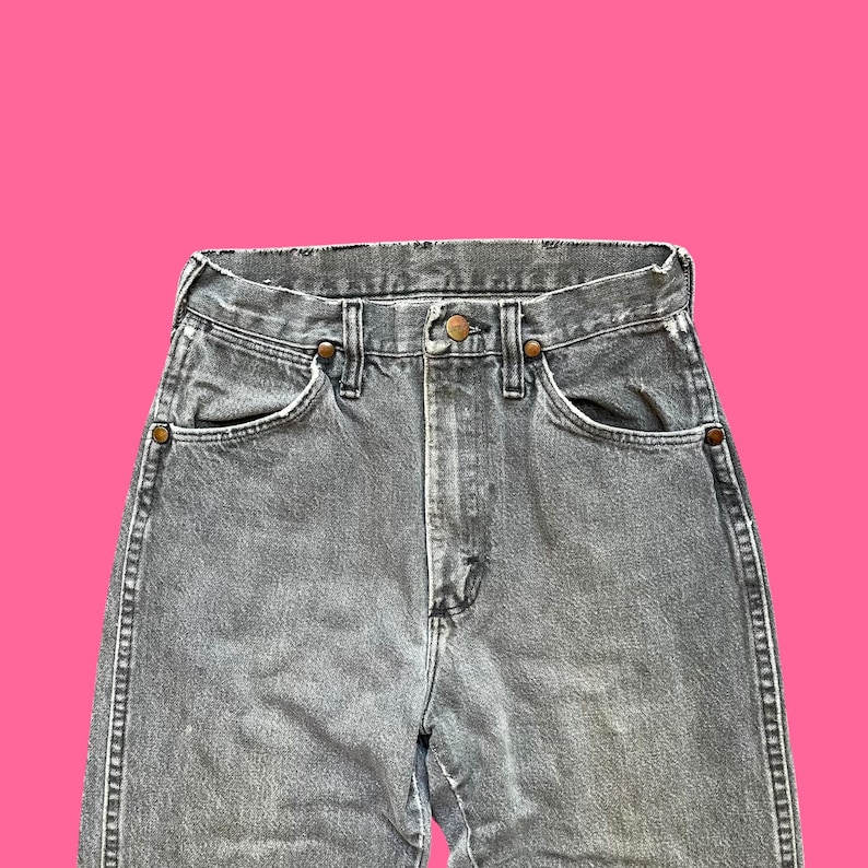 May include: Close-up of gray denim jeans with a high waist. The jeans have classic five-pocket styling, a button and zipper closure, and copper-colored rivets. The denim has a slightly faded appearance.