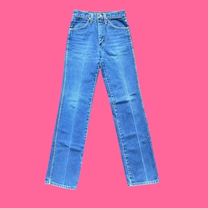 May include: Blue denim jeans with a classic five-pocket design. The jeans have a high waist and a straight leg fit. The denim is a medium wash with subtle fading and a slight sheen. The jeans are displayed against a pink background.