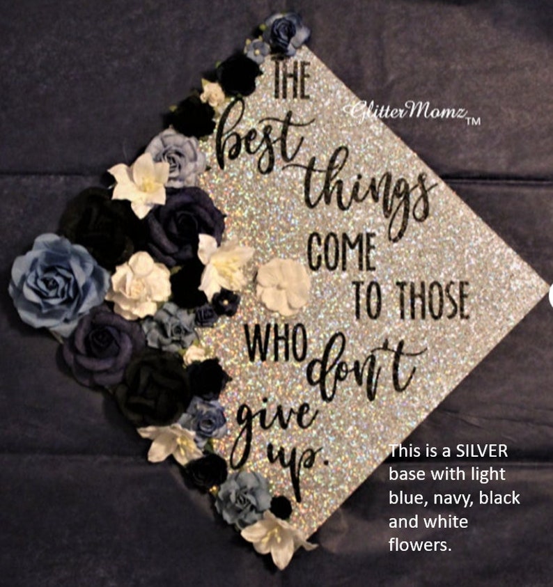 May include: A silver graduation cap decorated with blue, navy, black, and white flowers. The cap has the quote "The best things come to those who don't give up."
