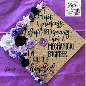 May include: A gold graduation cap decorated with purple and white flowers. The cap has a glitter finish and the text "I am not a princess. I don't need saving. I am a Mechanical Engineer. I've got this handled. BSME 2021" in black.