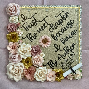 May include: Gold glitter graduation cap decorated with pink, white, and gold flowers. The cap has the quote "I trust the next chapter because I know the Author" and the date "Luke 1:37  00.2022".
