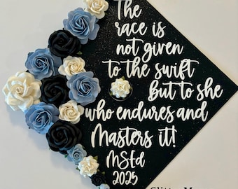 Peut inclure: Un chapeau de graduation noir orné de roses en papier bleues, noires et crème. Le chapeau porte la citation "The race is not given to the swift but to she who endures and Masters it!" et l'année 2025.