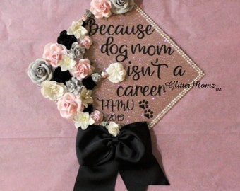 May include: A graduation cap decorated with pink, white, and gray flowers, a black bow, and the text "Because dog mom isn't a career" with the words "TAMU 2019" and paw prints below.