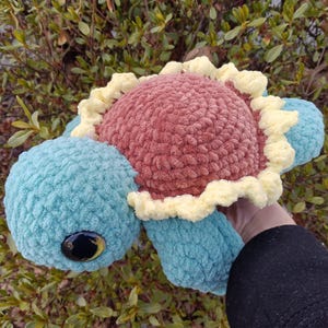 May include: A crocheted turtle toy with a blue body, pink shell, and yellow shell trim. The toy has large, black eyes with yellow pupils.