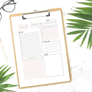 May include: A printable daily to-do list planner with sections for to-do, coming up, and notes. The planner is on a clipboard with a brown background.