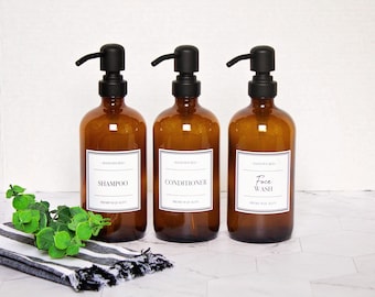 May include: Three amber glass bottles with black pump tops and white labels. The labels read "Shampoo", "Conditioner", and "Face Wash".
