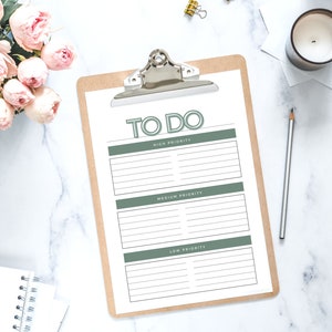 May include: A brown clipboard with a white sheet of paper that has the words "TO DO" written in green at the top. The paper is divided into three sections labelled "High Priority", "Medium Priority", and "Low Priority".