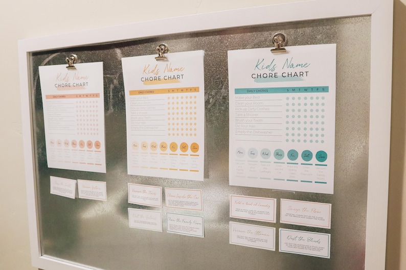 May include: Three printable chore charts with a colorful design and a grid for tracking daily chores. The charts are labeled "Kids Name Chore Chart" and include a list of daily chores and a grid for tracking completion. The charts are displayed on a metal surface with a white frame.