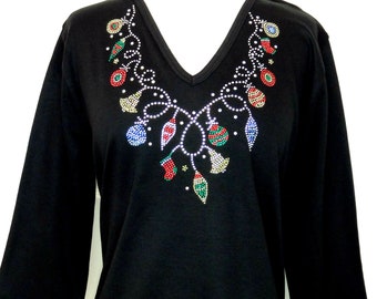 May include: Black long-sleeved shirt with a v-neck and a rhinestone design of a Christmas garland with ornaments and lights.