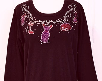 May include: A black long-sleeved shirt with a rhinestone design featuring a dress, shoes, and a purse.
