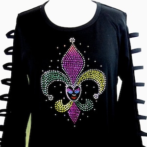 May include: Black long-sleeve shirt with a colorful rhinestone fleur-de-lis design on the front. The sleeves have cut-out details. The fleur-de-lis design features purple, green, yellow, and white rhinestones, creating a sparkling effect.