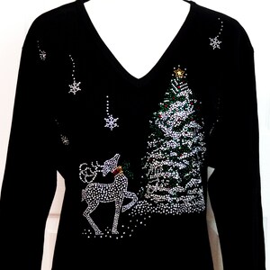 Pode incluir: Camiseta preta de manga comprida com um design de árvore de Natal e uma rena feito com strass. O design inclui strass verde, vermelho e branco.