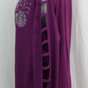 May include: A purple long-sleeved shirt with a floral design and rhinestones. The shirt has cutouts on the sleeves.
