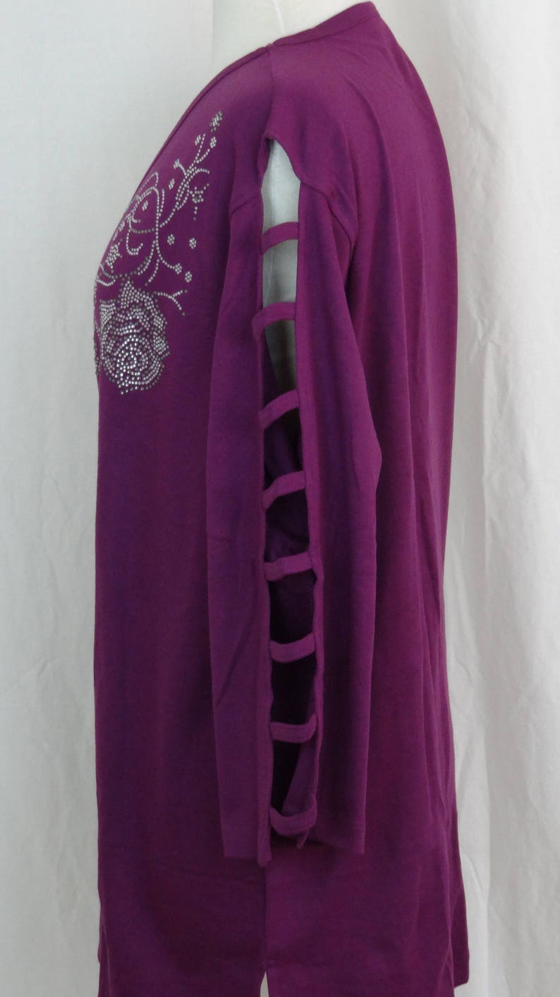 May include: A purple long-sleeved shirt with a floral design and rhinestones. The shirt has cutouts on the sleeves.