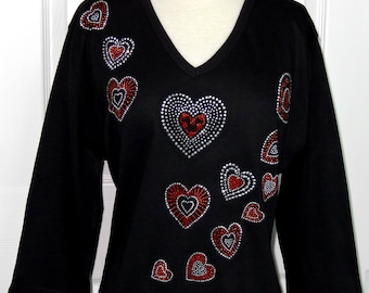 Puede incluir: Camiseta negra de manga larga con cuello en V y un diseño de varios corazones rojos y plateados hechos de pedrería.