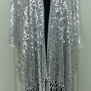 May include: A white sequined shawl with a fringe border. The shawl is open in the front and has a V-neckline.