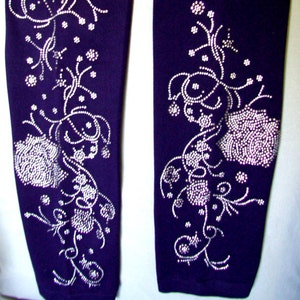 May include: A pair of purple leggings with a silver rhinestone floral design. The design features swirling vines and flowers.