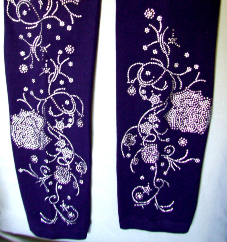 May include: A pair of purple leggings with a silver rhinestone floral design. The design features swirling vines and flowers.