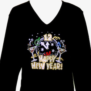 Könnte beinhalten: Schwarzes Langarm-V-Ausschnitt-Shirt mit Strass-Design. Das Design zeigt ein Zifferblatt mit den Zeigern auf Mitternacht, zwei Martinigläser und die Worte "HAPPY NEW YEAR!"