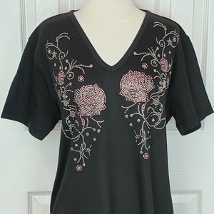 May include: Black short-sleeved t-shirt with a v-neck and a floral design made of rhinestones. The flowers are pink and the leaves are silver.