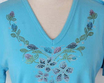 Blusa de malha com decote em V, manga 3/4 ou curta, estampa floral e de folhas em cascata com aplicações de strass. Disponível nos tamanhos P ao 3XG.