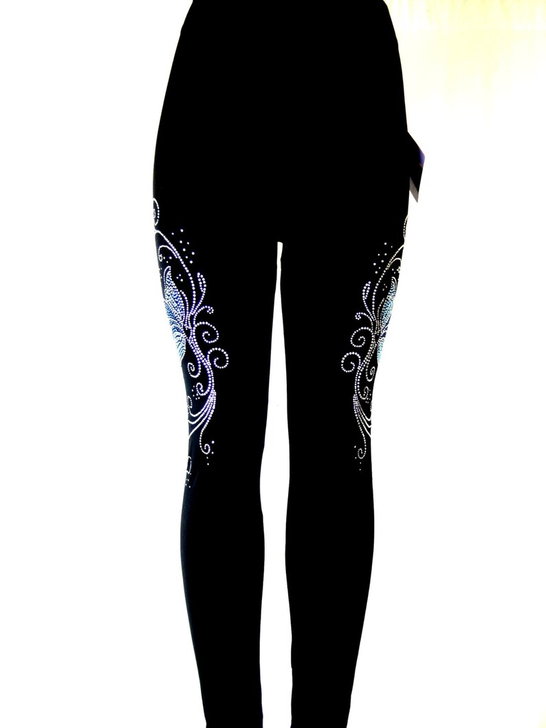May include: Black leggings with a rhinestone design on each leg. The design features a stylized butterfly with swirls and dots.