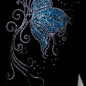 May include: A black fabric with a blue and silver rhinestone butterfly design. The butterfly is surrounded by swirls and dots.