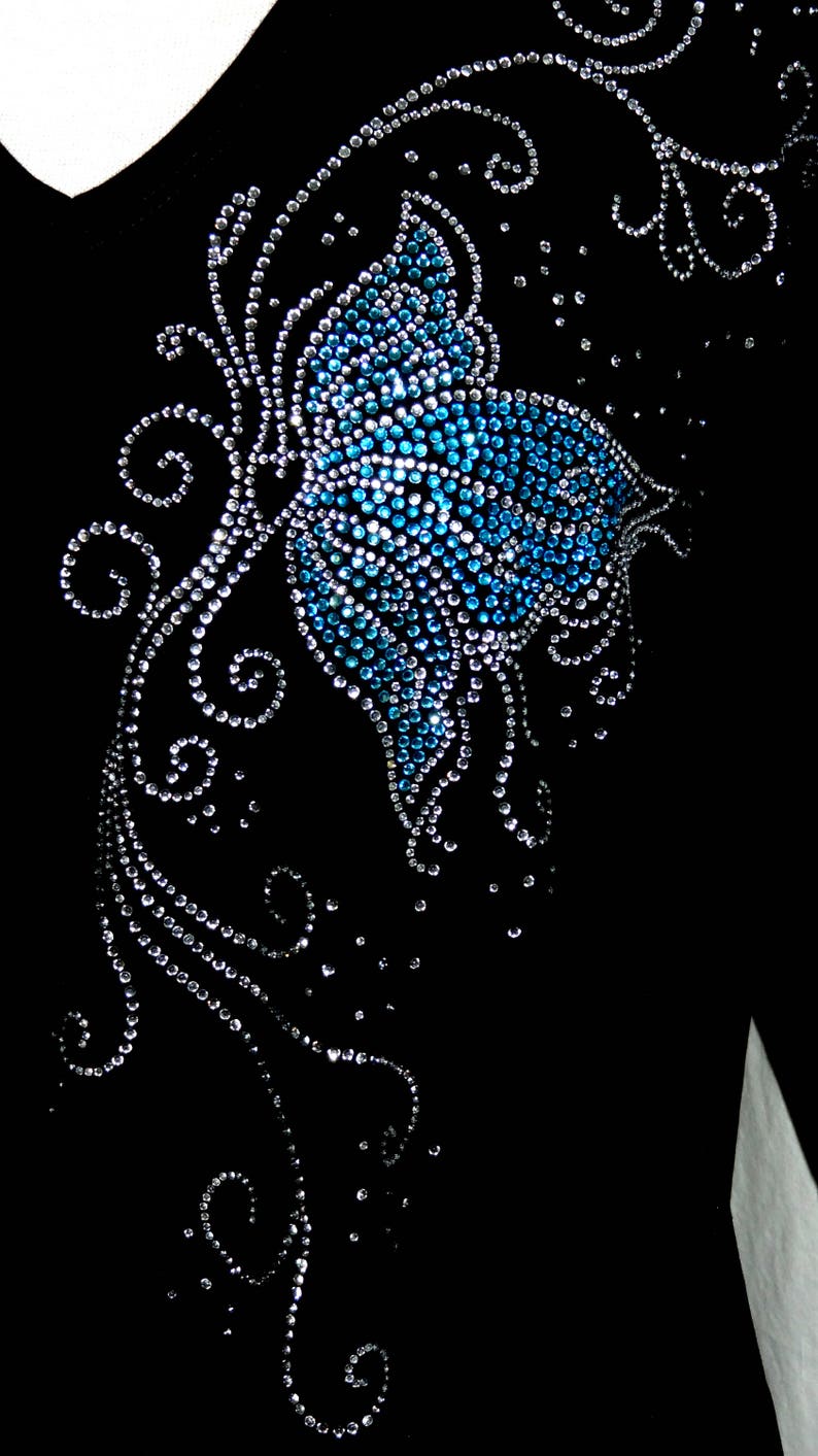 May include: A black fabric with a blue and silver rhinestone butterfly design. The butterfly is surrounded by swirls and dots.