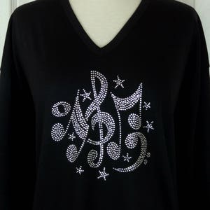 May include: Black long-sleeved shirt with a rhinestone design of musical notes and stars.