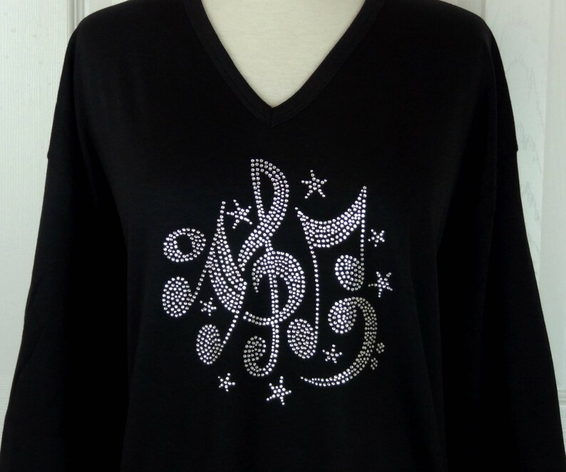 May include: Black long-sleeved shirt with a rhinestone design of musical notes and stars.