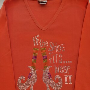 May include: Orange long-sleeved shirt with a sparkly design of two witch's shoes and the text "If the shoe fits... wear it".