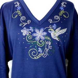 May include: A navy blue long-sleeved shirt with a rhinestone hummingbird and floral design. The design features green, blue, and white rhinestones.
