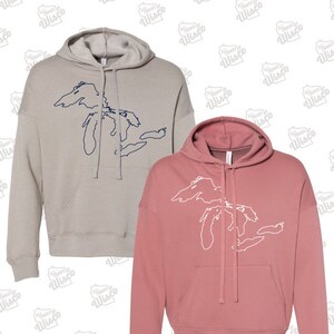 May include: Two hooded sweatshirts with a graphic of the Great Lakes. One sweatshirt is a light gray color with a navy blue outline of the Great Lakes. The other sweatshirt is a dusty rose color with a white outline of the Great Lakes.