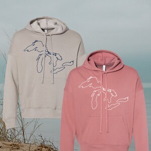 May include: Two hooded sweatshirts with a graphic of the Great Lakes on the front. One sweatshirt is light gray with a navy blue graphic, and the other is a dusty rose color with a white graphic.