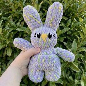May include: A handmade crochet bunny in shades of purple, yellow, and green. The plush toy has long ears, a yellow beak, and black eyes. The bunny is soft and cuddly, perfect for a child's toy or nursery decor.