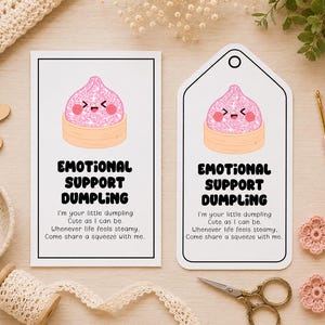 May include: Two white paper cards featuring a pink glittery dumpling illustration with a smiling face. The text reads: EMOTIONAL SUPPORT DUMPLING. I'm your little dumpling. Cute as I can be. Whenever life feels steamy, Come share a squeeze with me.