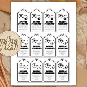 May include: A sheet of white paper with twelve black and white security tags. Each tag has a cartoon eye design and the text "AVISO DE SEGURIDAD". A circular label reads "12 ETIQUETAS POR HOJA DE 8.5 X 11 PULGADAS".